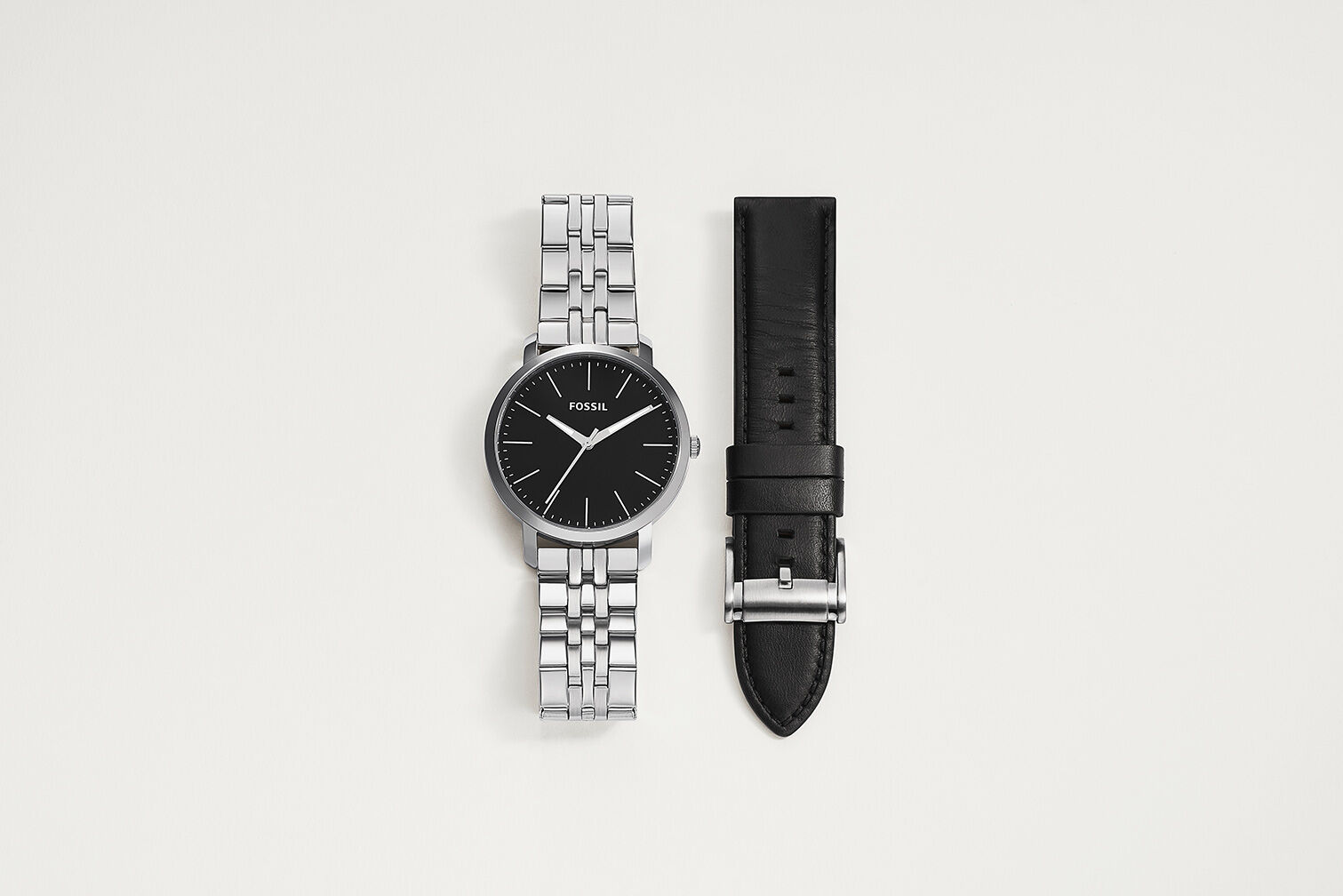 A silver men's stainless steel watch lying next to a leather interchangeable watch strap.