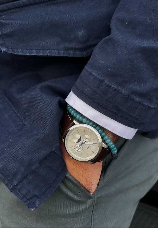 Ein Mann mit einer goldfarbenen Uhr mit Himmels-Tracker und einem Bead‑Armband.