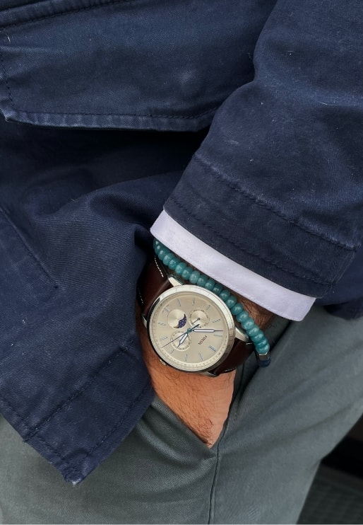 A man wearing a gold-tone Celestial watch with a beaded bracelet.