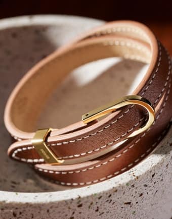 Un bracelet en cuir brun avec des garnitures métalliques à maillon en D ton or.