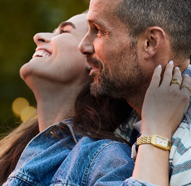 A couple smiling and embracing in the sun. The woman is wearing the gold-tone Fossil Raquel mini watch.