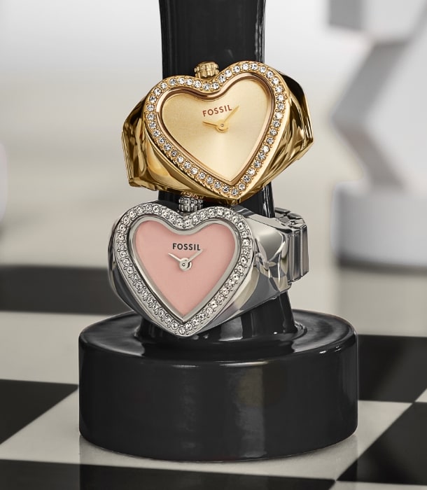 A gold-tone watch ring and a silver-tone watch ring stacked on top of a black chess piece on a chess board.
