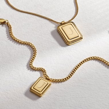 Due collane color oro con charm a forma di lettera.