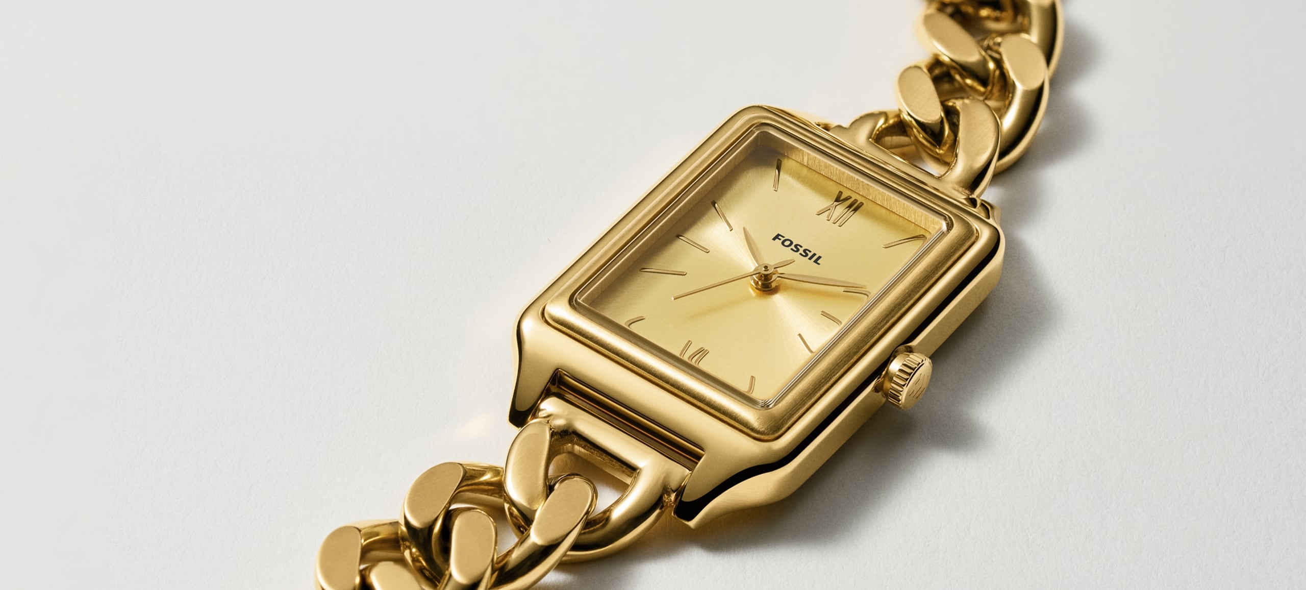 A gold-toned Fossil Raquel chain watch lies on a white background.