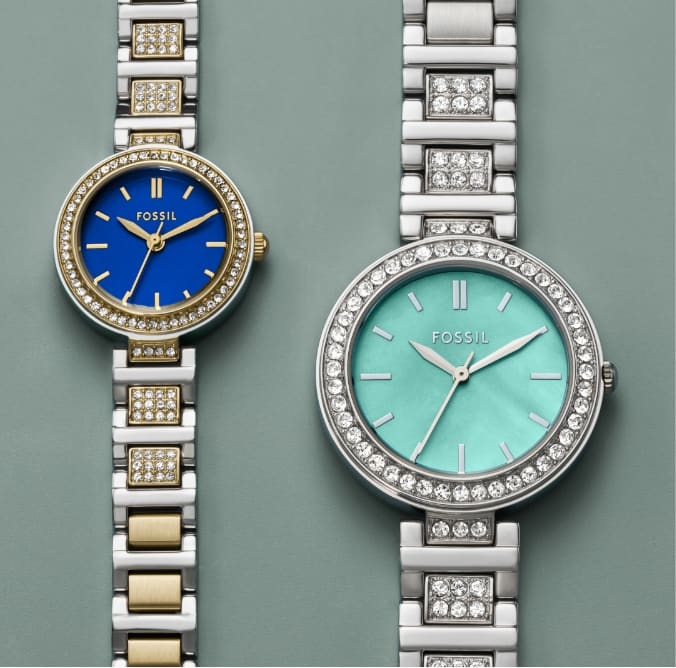 Zwei Damenuhren nebeneinander, beide mit rundem Zifferblatt, funkelnder Lünette und funkelndem Band. Die linke Uhr ist kleiner mit einem himmelblauen Zifferblatt, die rechte Uhr ist größer mit einem aquablauen Zifferblatt.