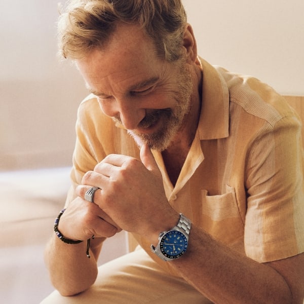 Un homme souriant et portant la montre Fossil Blue GMT ton argent avec un cadran bleu.