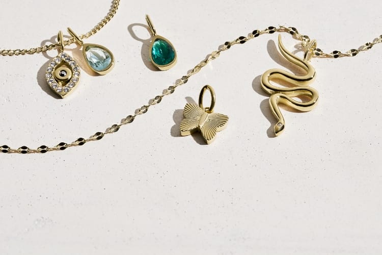 Cinco charms en tono dorado y dos cadenas en tono dorado.