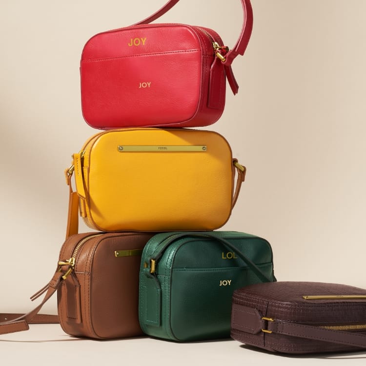 A stack of Liza Camera Bags in multiple colours. The first one embossed with the word JOY.