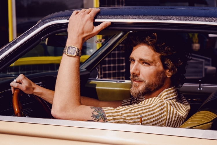A man looking out the window of a vintage car, wearing a watch with a square case.
