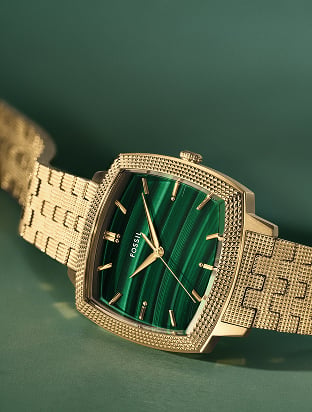 Image of gold-toned Fossil x Nick Jonas watch on green background.