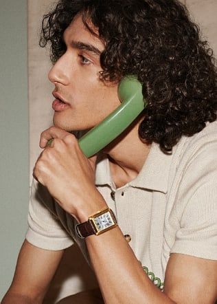 Un hombre con un reloj Carraway de piel marrón que sostiene un auricular de teléfono verde. 