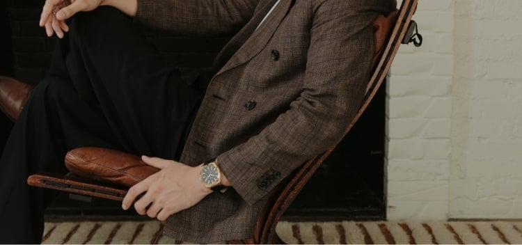 A man posing in a chair and wearing a black and gold-tone Fossil watch. 