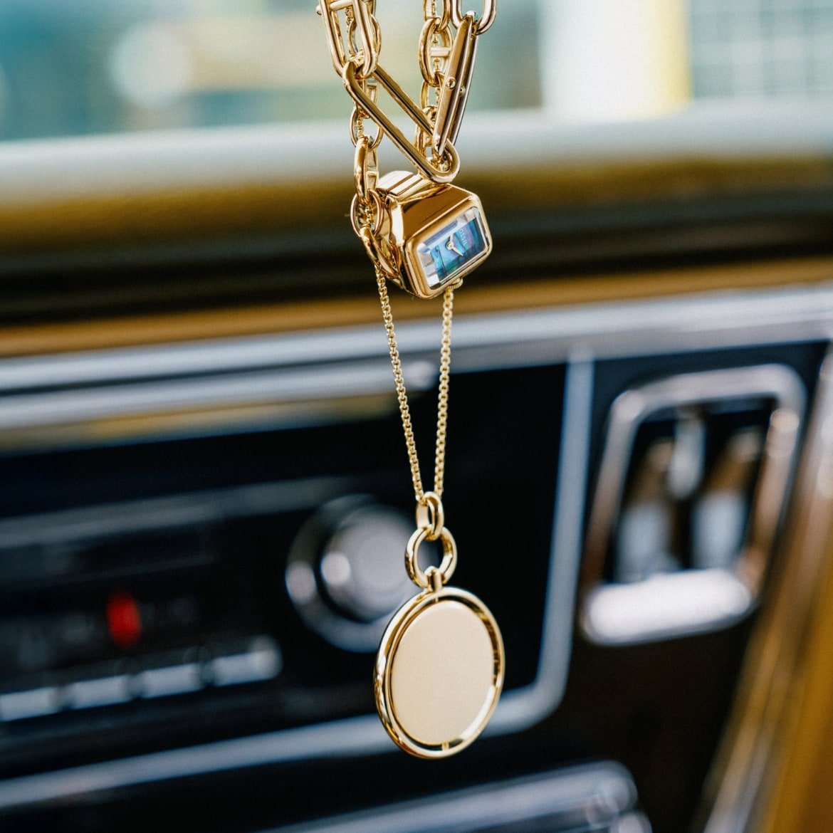 A mix of gold-tone jewellery hangs from the rear-view mirror of a car.