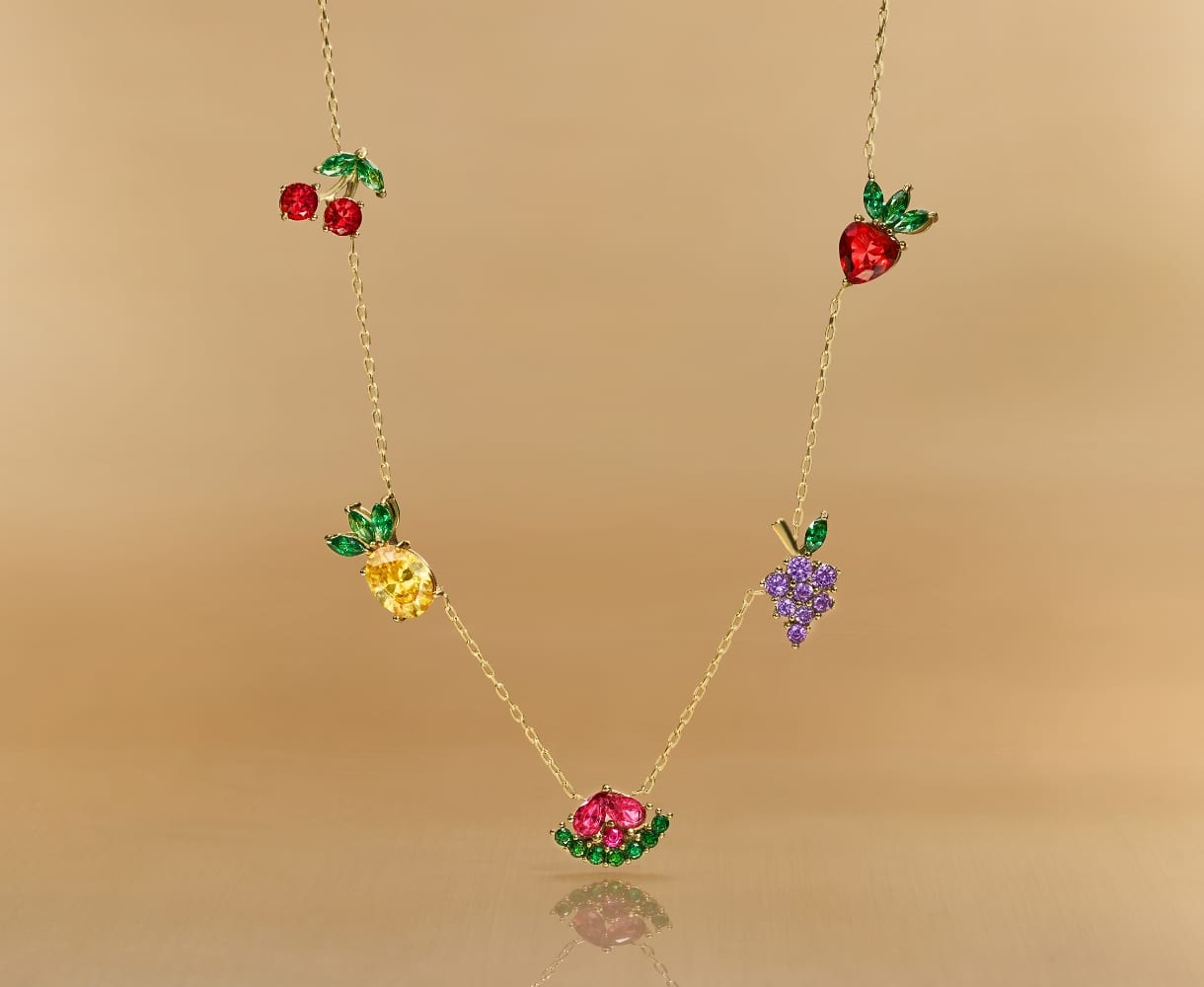 Una cadena en tono dorado con detalles de cinco cristales en forma de fruta.