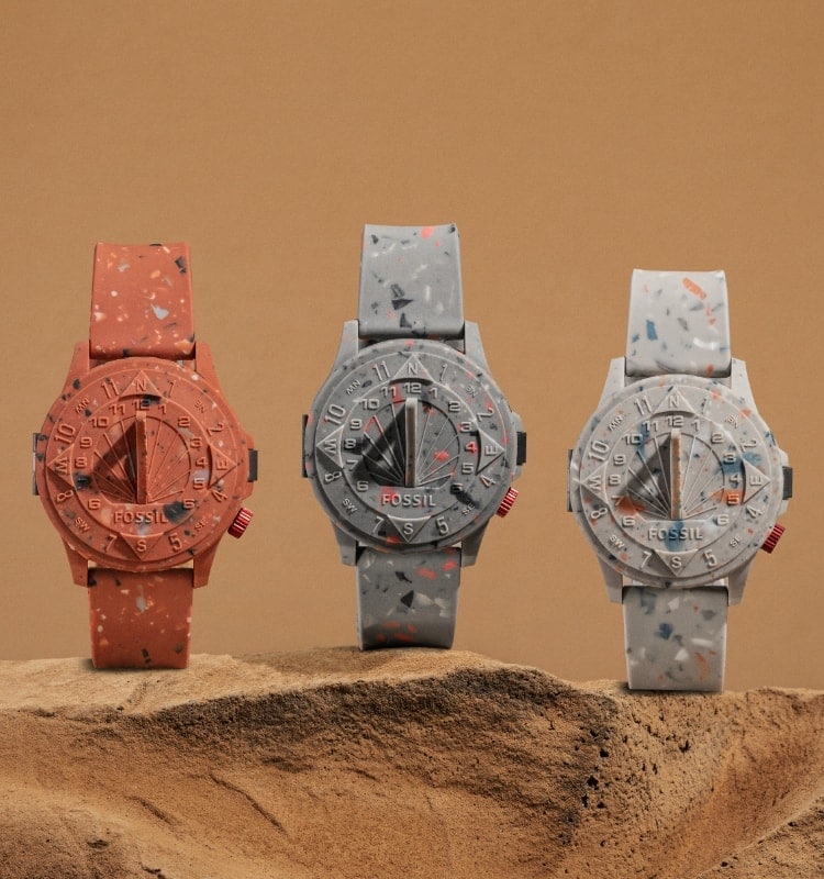 Three STAPLE x Fossil watches sitting in dirt.