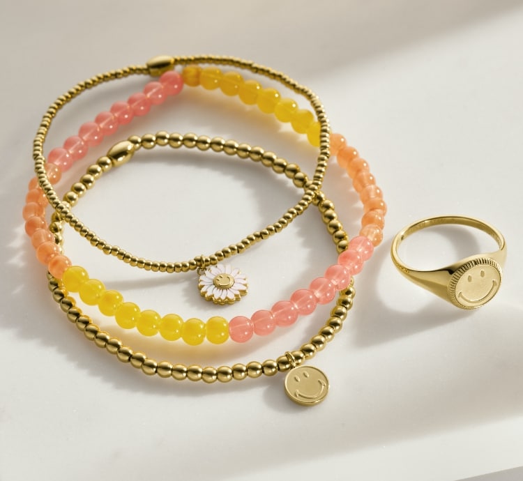 Gold-tone and beaded Fossil x Smiley jewellery. Smiling daisy graphics.