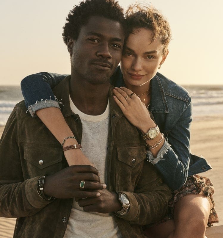Un homme et une femme enlacés sur une plage et portant des modèles de la collection Fossil Heritage.