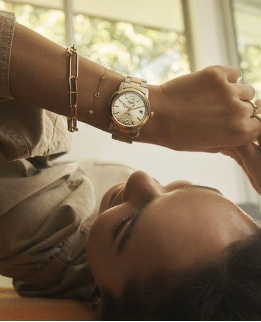 Immagine di una donna sdraiata che guarda il suo orologio Fossil Heritage bicolore.