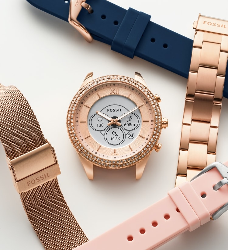 Un cadran de montre connectée Gen 6 hybride et différents bracelets interchangeables, comprenant des bracelets en acier inoxydable doré, en maille milanaise rose poudré, en silicone bleu marine et en silicone rose poudré.