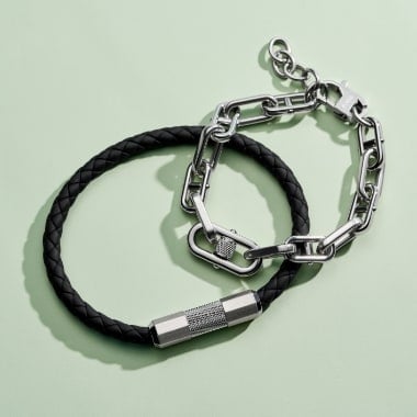 Two men's bracelets: one black leather with a textured metal accent and one D-link chain.