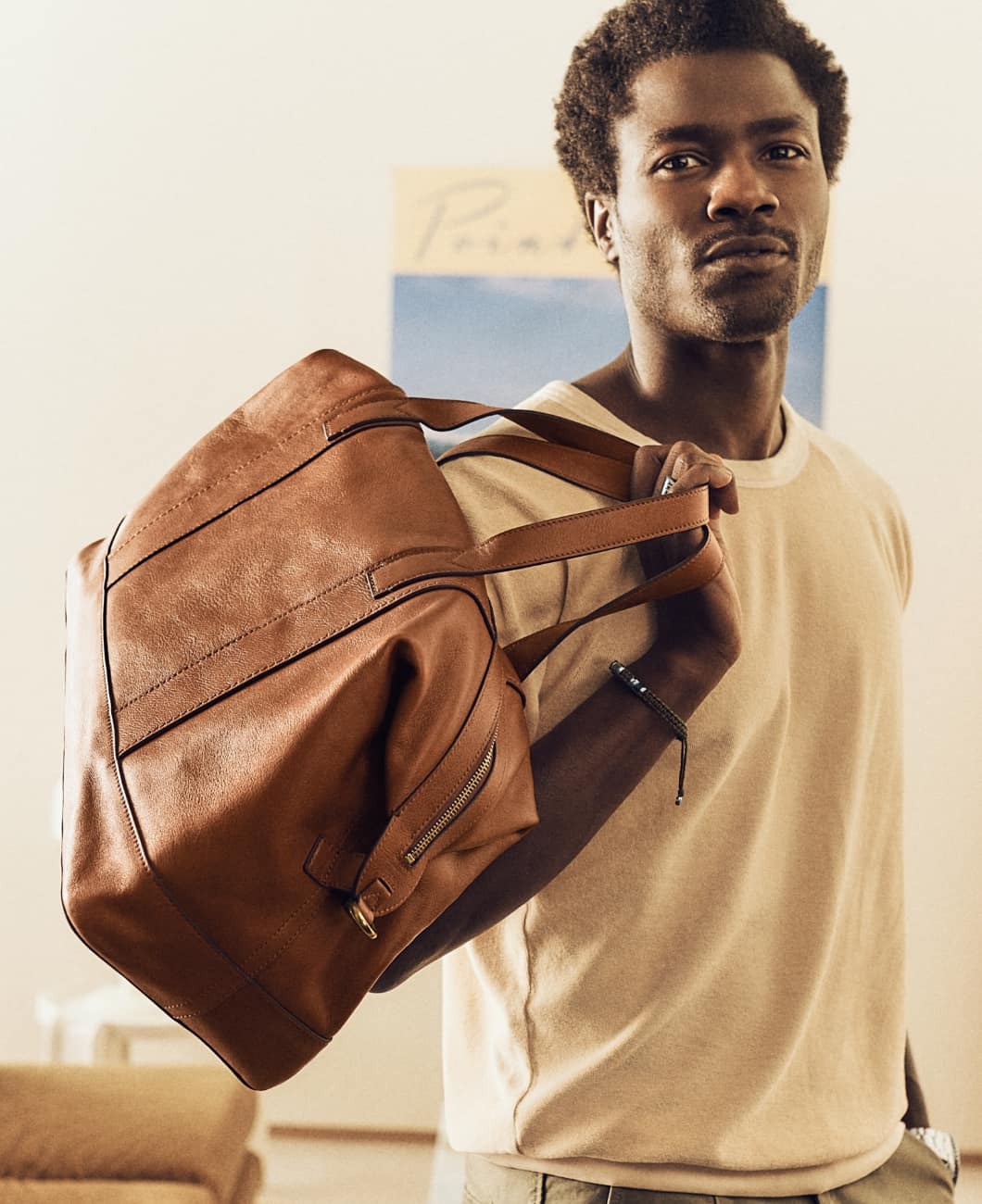 A man stands boldly with the Raeford duffle tossed over his shoulder. It has soft brown leather, a lightweight, convertible silhouette and a removable and adjustable crossbody or shoulder strap.