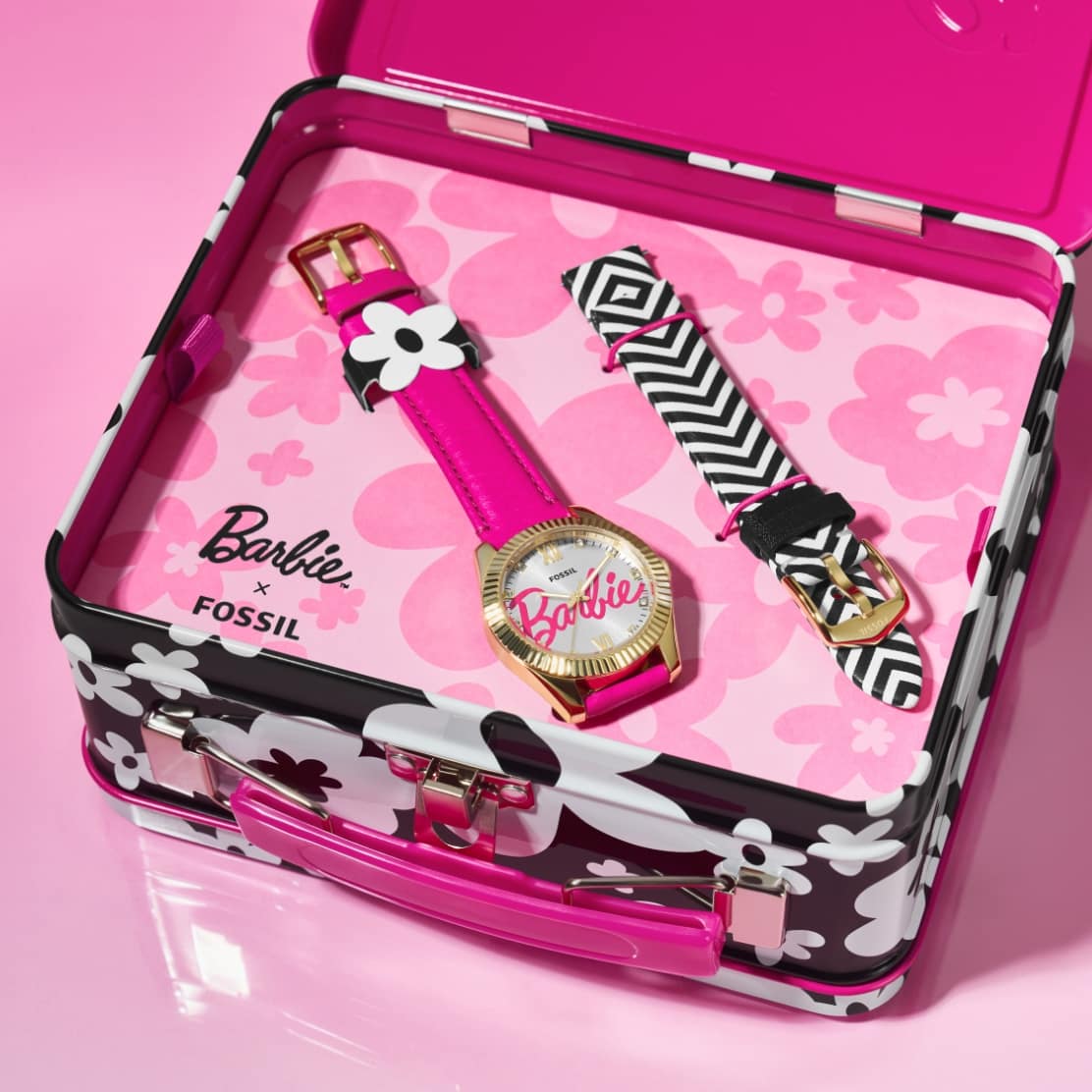 Image two. The tin is shown open to reveal a special-edition watch set inside. It features the scripted Barbie signature on the dial and leather strap in hot pink, displayed with interchangeable leather straps in a black-and-white chevron pattern.