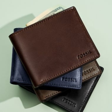 A stack of four leather wallets embossed with the Fossil logo.
