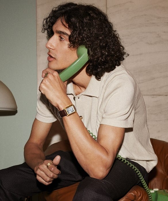 Un uomo che indossa un orologio Carraway con cinturino in pelle marrone e ha in mano una cornetta del telefono verde. 