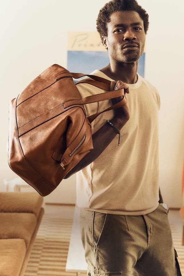 Un homme portant un sac de voyage Raeford en cuir marron.