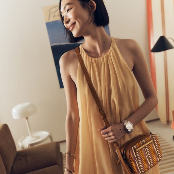 A woman in a yellow dress wearing the Liza camera bag in colourful woven leather.