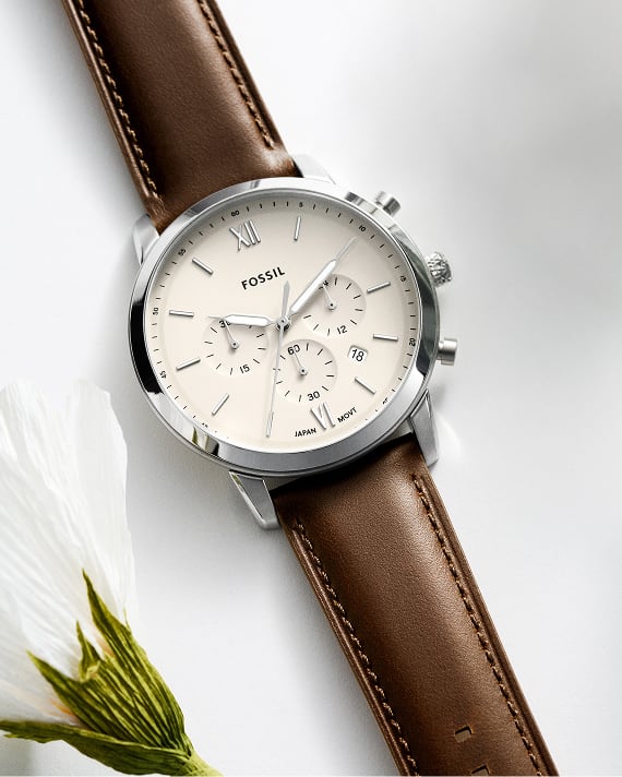 Fossil Herrenuhr Neutra mit braunem Lederband und weißem Zifferblatt neben einer Blume