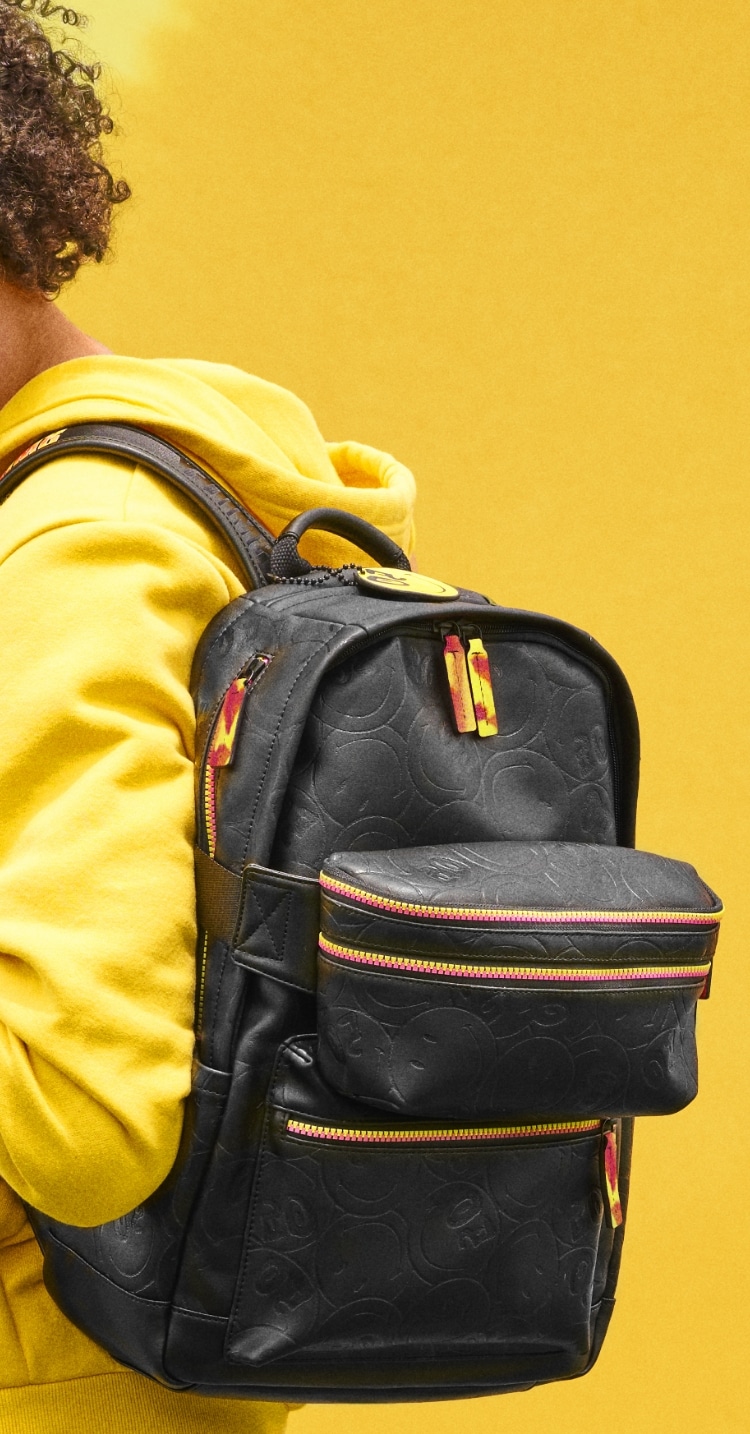 Man wearing a yellow sweatshirt carrying the black limited edition Smiley backpack. Smiley face logo.