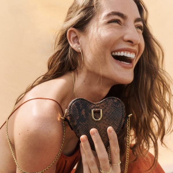 A woman holding a heart-shaped, python-embossed leather micro bag.