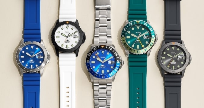 Cinq montres inspiration plongée pour homme sont présentées de gauche à droite dans les couleurs suivantes : bleu, blanc, argenté avec cadran bleu, vert d’eau et gris.