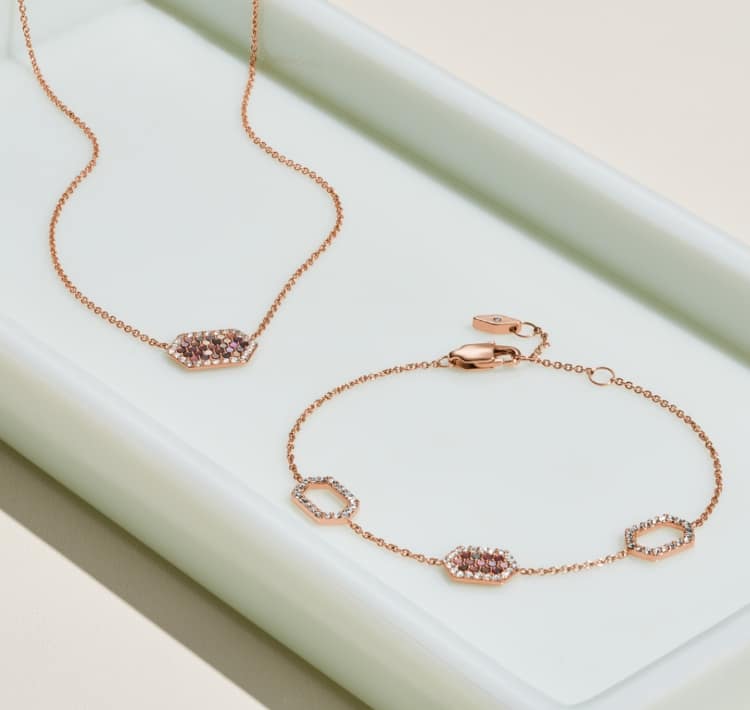 A necklace and bracelet are displayed on a long white tray. The jewellery has a rose gold-tone with sparkling crystals in a hexagon shape.