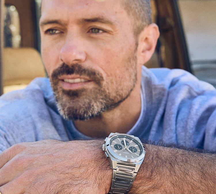 A casually dressed man looking into the distance, wearing the Fossil Everett Chronograph watch in a stainless steel finish.