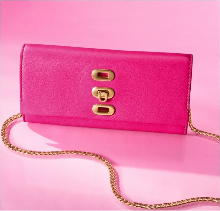 Ein pinker Hintergrund mit einem Fenster im Stil des Traumhauses von Barbie™. Im Fenster sieht man unsere Limited Edition Barbie™ x Fossil Kameratasche Liza aus glattem Leder im typischen Pink mit extrabreitem, sportlichem Riemen im 90er-Jahre-Stil mit pinken Streifen.
