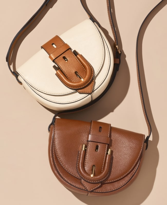 A woman lounges on a soft brown couch with her Liza camera bag in hand. It features an adjustable strap and a woven leather pattern in bright, punchy colors.
