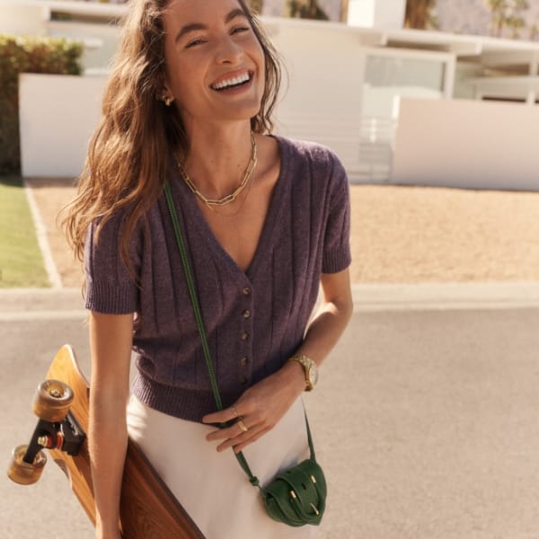 A woman carrying a skateboard and wearing the green python-embossed micro crossbody bag.