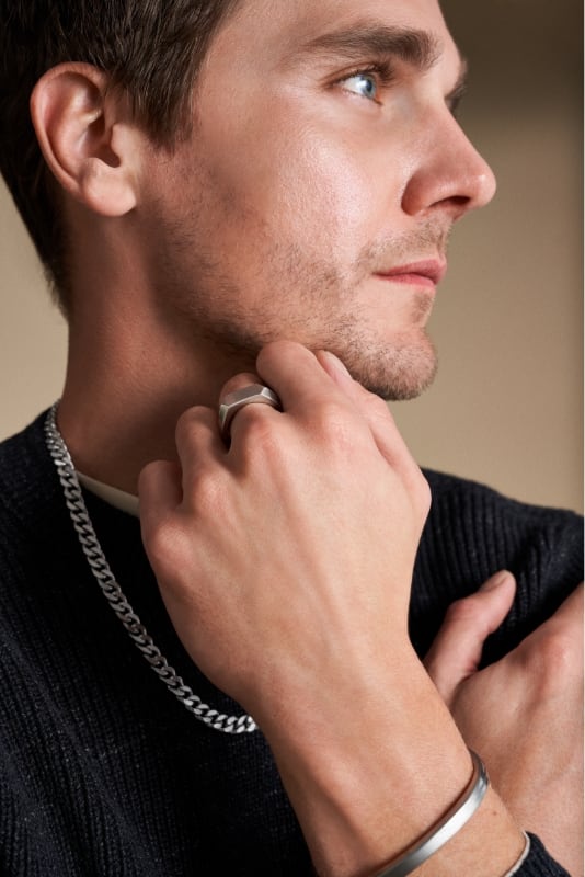 A man in a black shirt wearing silver-tone Fossil jewelry.