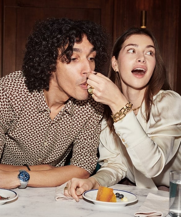 A man and a woman eating cake and wearing styles from the fall 2023 collection. 