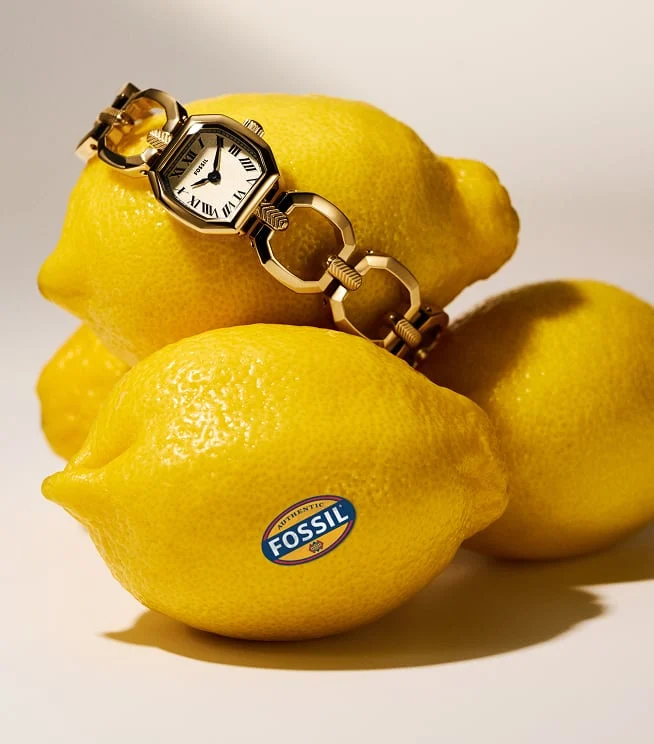 The Fossil Harlow chain bracelet watch is playfully placed over fresh lemons. Fossil fruit stickers add a fun accent.