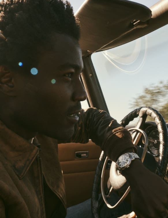 Un uomo alla guida di un’auto indossa un orologio Fossil Heritage.