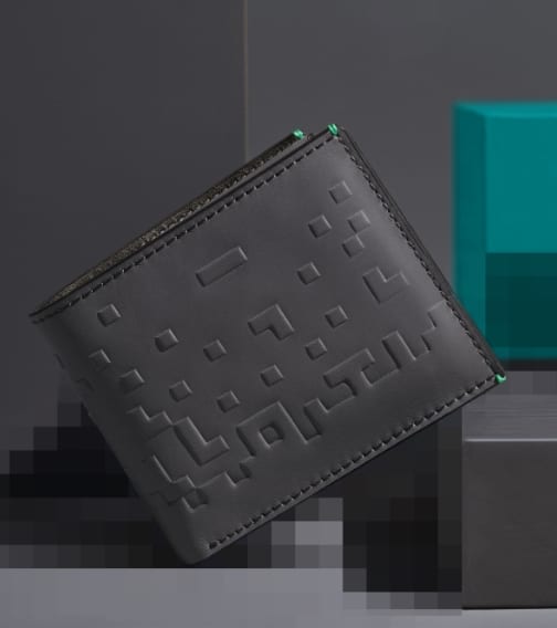 Un portefeuille en cuir gris foncé marqué d’une texture pixellisée sur des blocs gris ton sur ton.