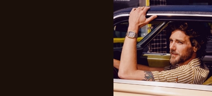 A man looking out the window of a vintage car, wearing a watch with a square case.