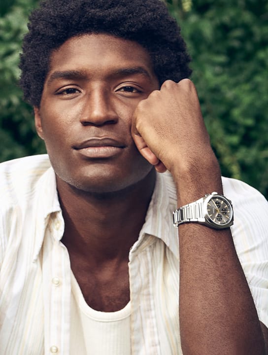 A man casually sitting, wearing the architectural Fossil Carraway watch.