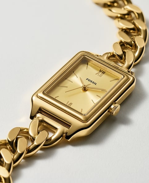 A gold-toned Fossil Raquel chain watch lies on a white background.