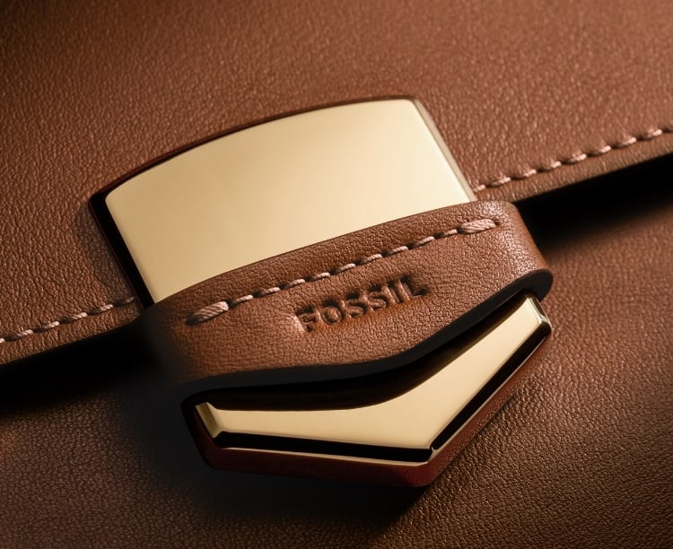 The gold-tone Fossil Crest on the brown leather Lennox bag, overlaid with a sketch of the Crest.