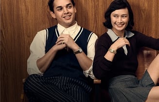 A preppy couple sits together in front of a wood-panelled wall wearing Fossil watches.