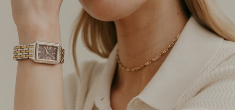 A woman wearing the two-tone Raquel watch with brown dial and gold-tone Fossil jewelry.